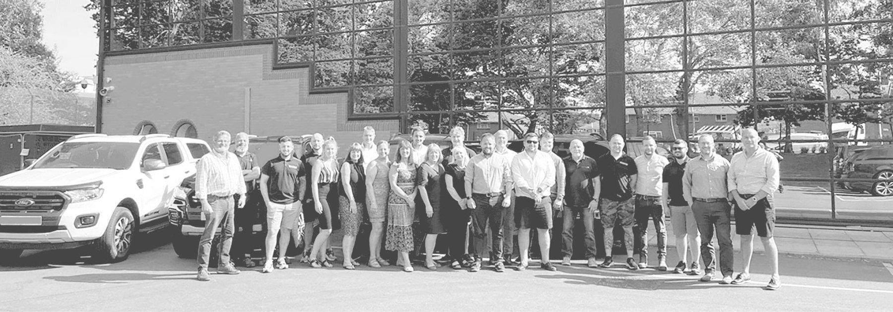 Greyscale group shot of happy staff outside Sealpac UK & Partners HQ